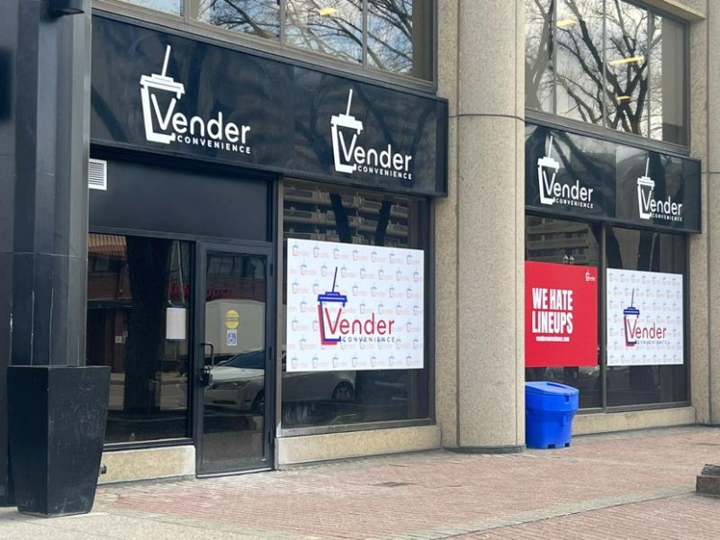 The outside of Vender Convenience as seen from the sidewalk, with windows sporting signs that say "Vender" and "We Hate Lineups"