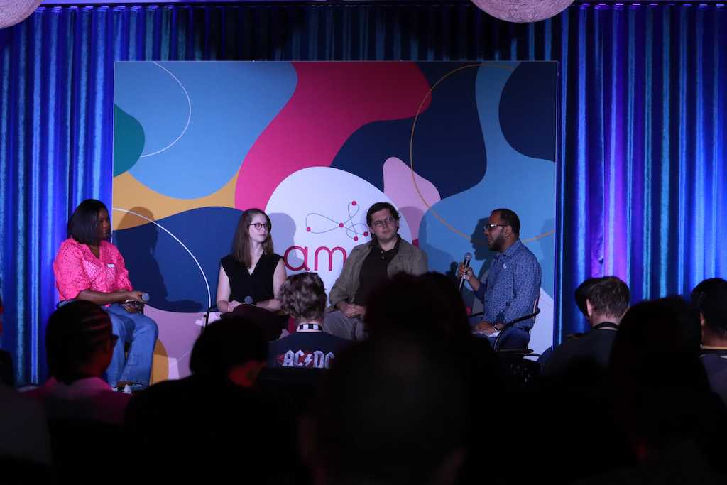 <p>Host Deborah Akaniru sits to the left of panelists Breanna Duffy, Michael Todhunter, and Sheikh Jubair, who is speaking. They sit in a row in front of a multi-coloured Amii sign and blue curtains.</p>