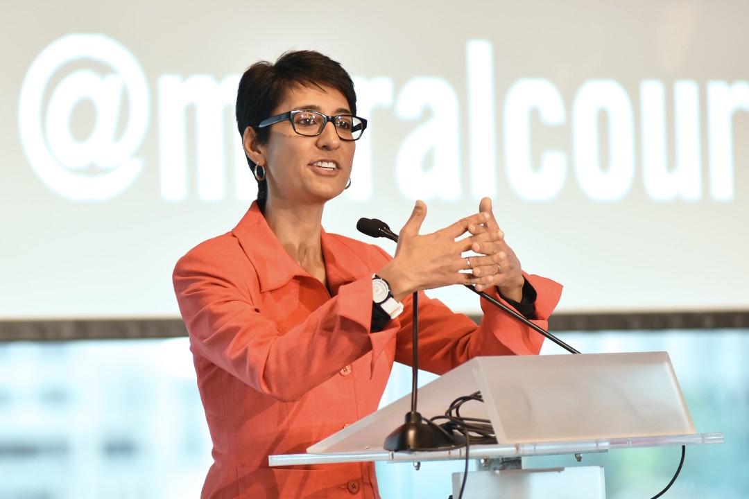 Irshad Manji speaks at a podium, her hands meshing together in front of her