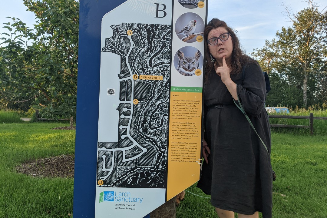 Kyla Tichkowsky leans against a Larch Sanctuary sign while pointing her finger to her chin