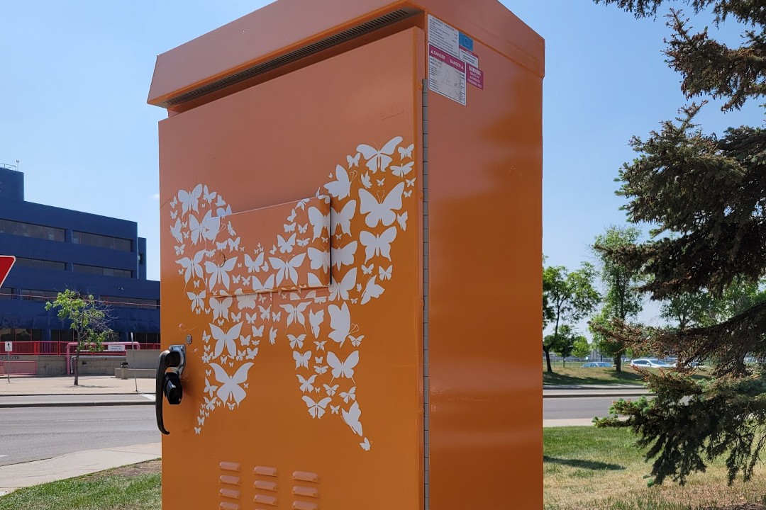 Traffic control box painted orange and adorned with small white butterflies arranged in the shape of a larger butterfly