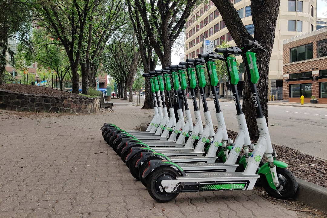 A row of 11 Lime e-scooters arranged neatly along a downtown Edmonton sidewalk