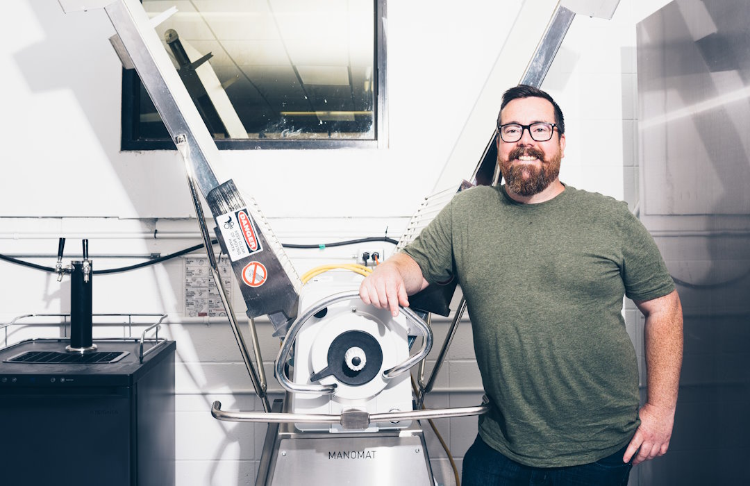 Uproot Food Collective co-founder and CEO Chris Lerohl poses to the right of a food-manufacturing tool.