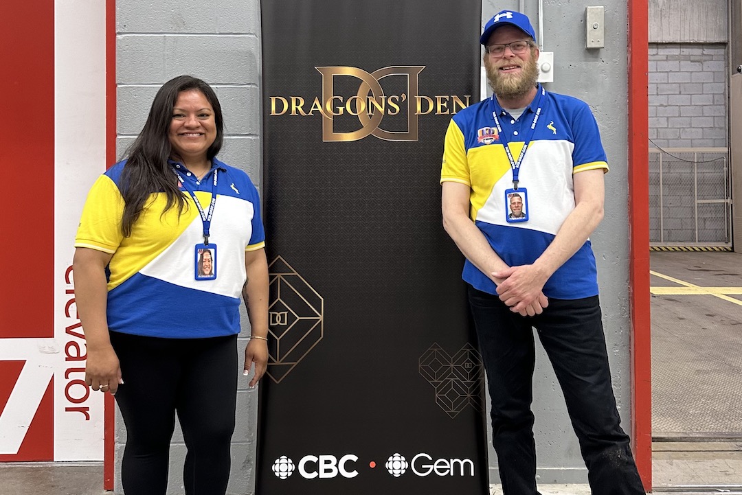 Kid-Drop co-founders Julieta Miranda and Josh Kalhofer pose on opposite sides of a promotional banner for Dragons' Den.