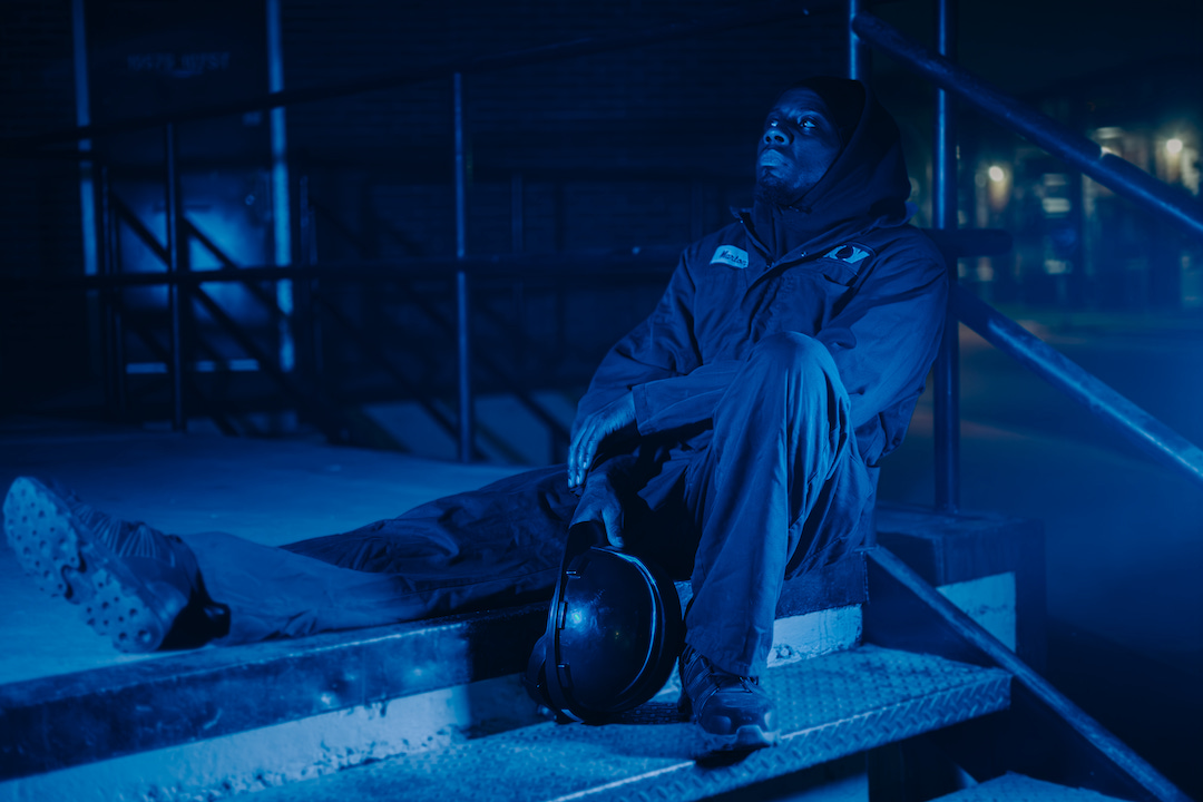 Rapper Arlo Maverick splays across a stoop, lit in blue under the cover of dark.