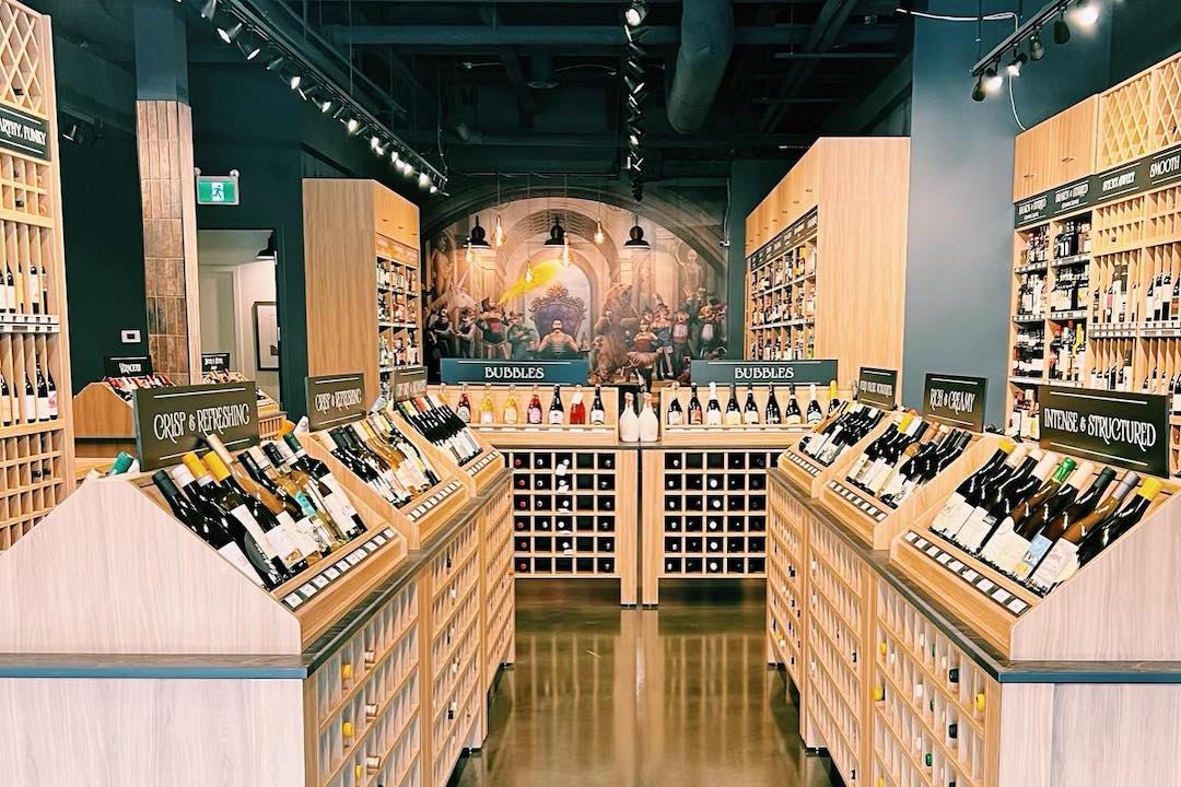 The interior of Vine Arts Wine and Spirits includes many shelves stocked with bottles and, in the background, a mural depicts humans and creatures standing in a row