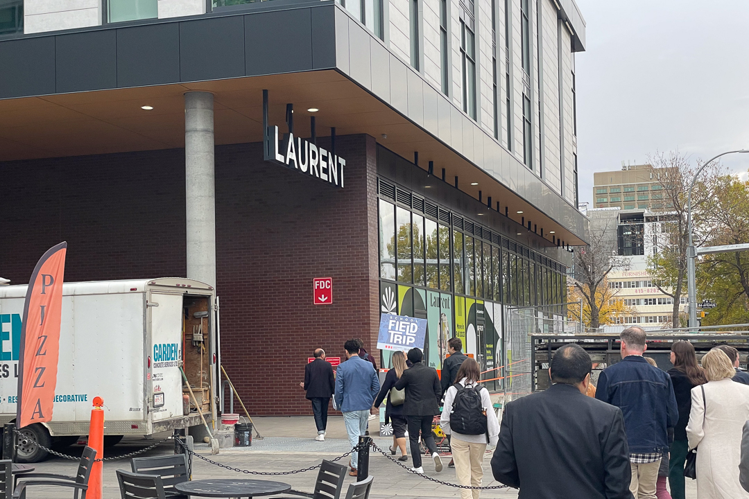 A group of people file into the entrance of a dark, glass and brick building.