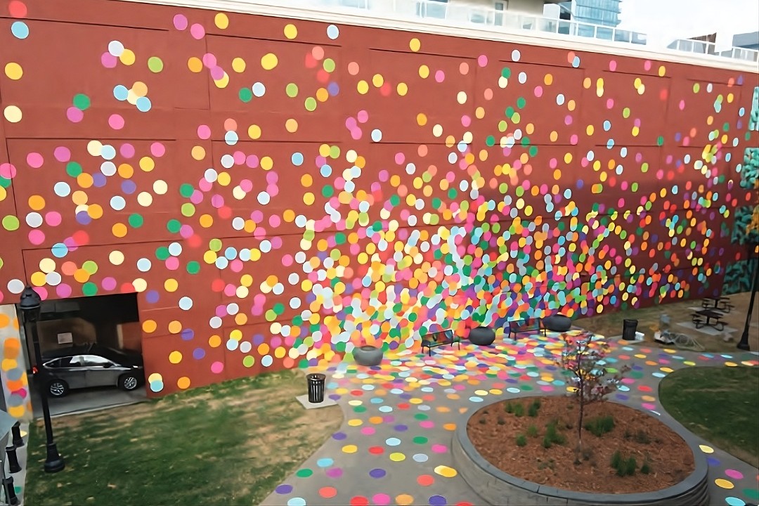 A small downtown park overlooked by a large red wall covered in an array of multicoloured dots