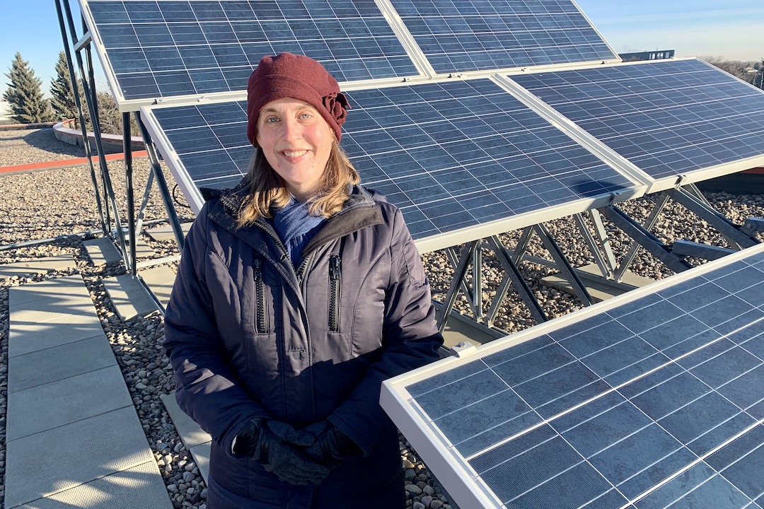 Heather MacKenzie smiles while surrounded by solar panels set up in an array