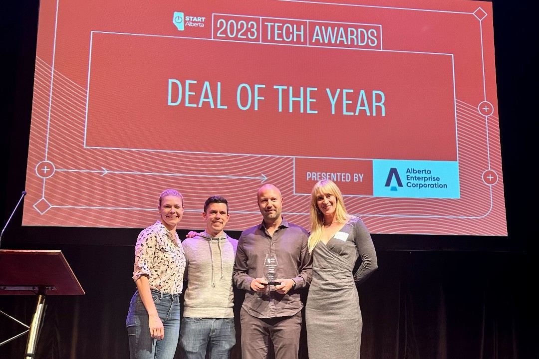 Four smiling people stand in front of a slide reading "2023 Tech Awards: Deal of the Year, presented by Alberta Enterprise Corporation"