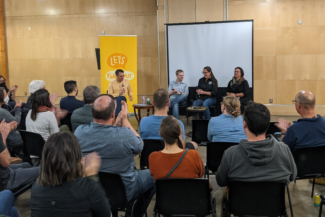 An audience applauds as four people in front of the room smile, with the Let's Find Out banner behind them