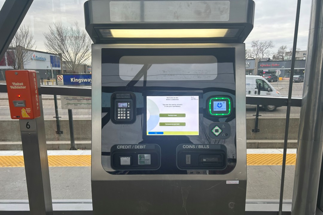 A paper ticket validator next to a modern Arc fare machine inside a shelter at an LRT station.