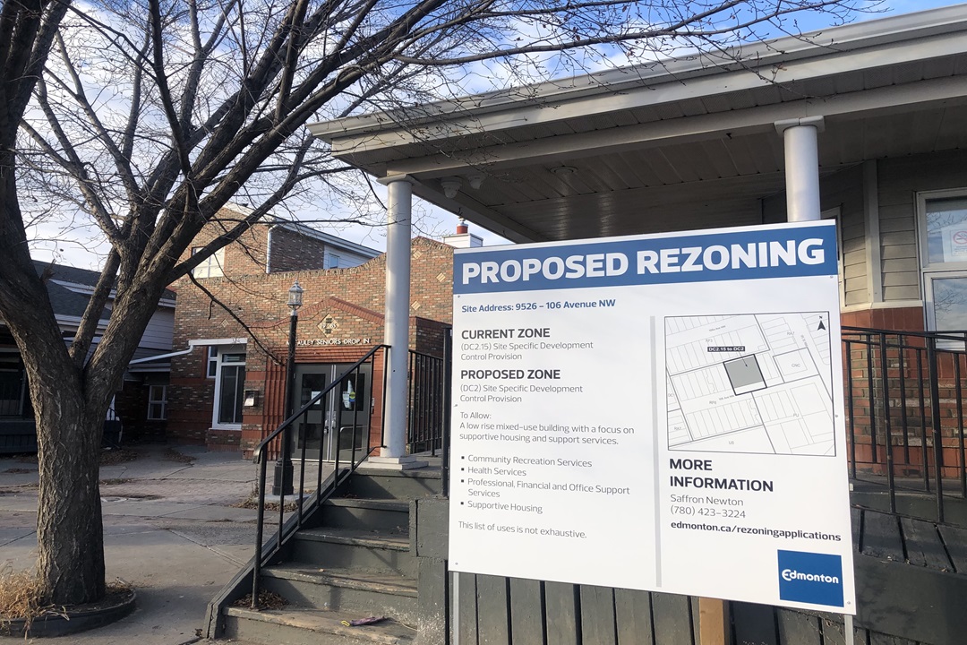 A rezoning sign in front of a brick building in Edmonton's McCauley neighbourhood.