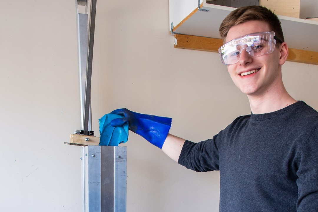 A smiling man wearing safety glasses operates a tool that breaks down plastic for recycling.