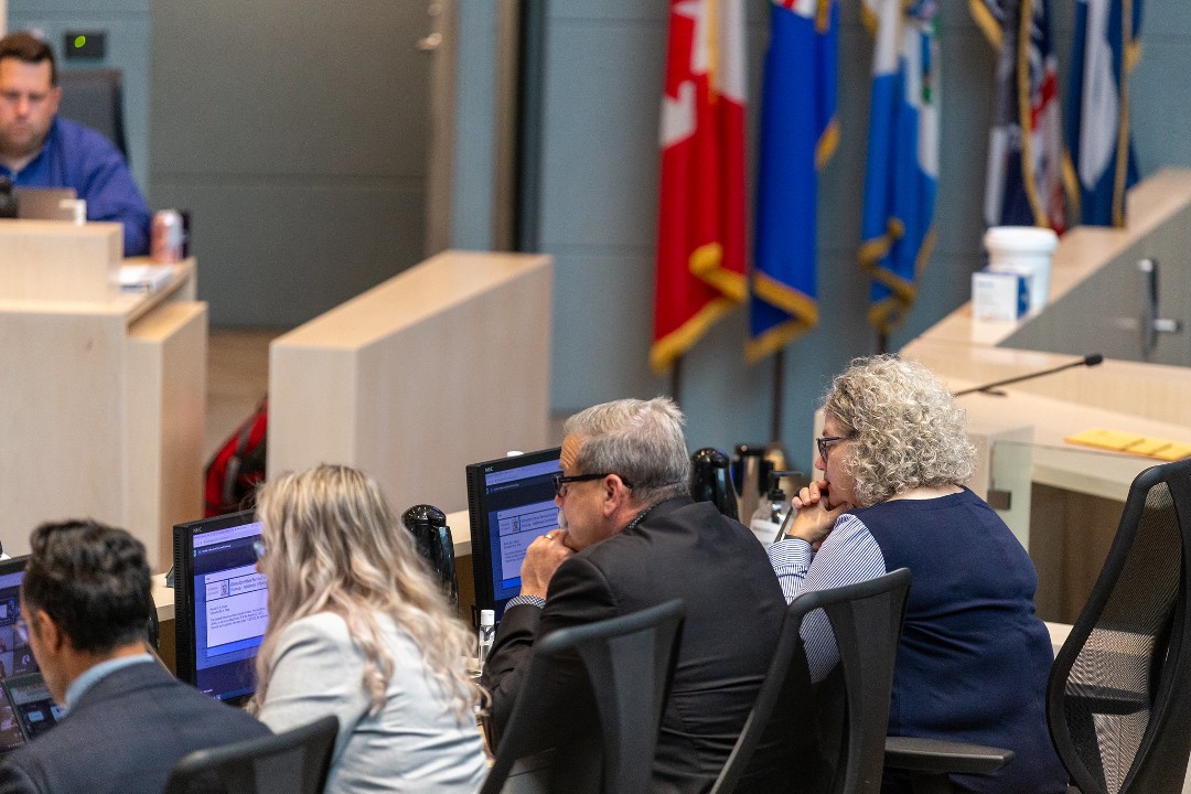 Several people sit before a desk with microphones, facing toward Edmonton city council.