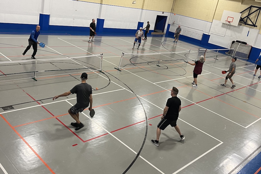 Three games of pickleball take place inside a gym.