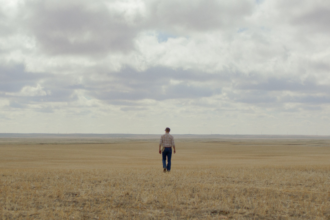 A person walking in a vast field with a cloudy sky.