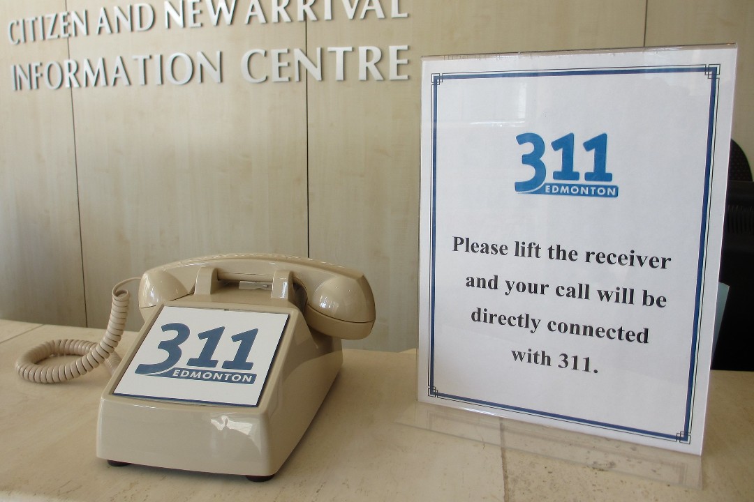 A beige phone with a sign over its number pad that reads "311 — Please lift the receiver and your call will be directly connected with 311."