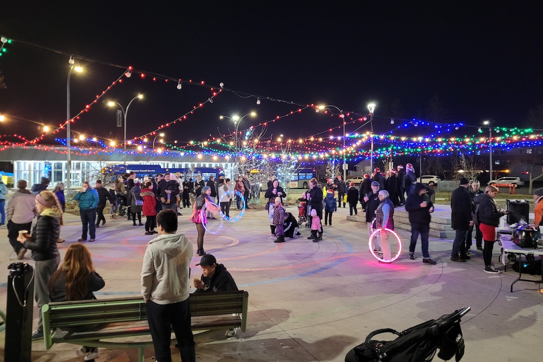 A large outdoor crowd gathered under holiday lights in an outdoor square.