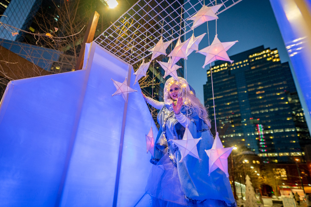 A person dressed as a winter princess with illuminated stars hanging above them.