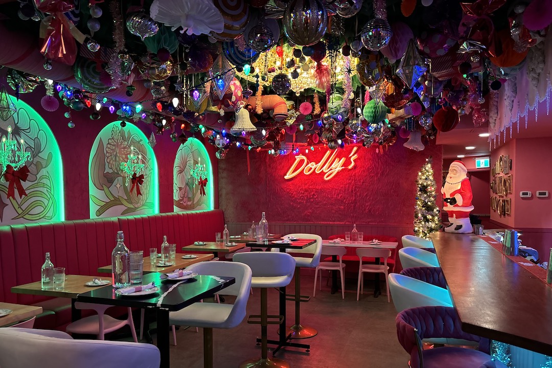 A vibrant restaurant interior shows a large amount of Christmas decorations, tables, chairs, a bar, and a sign reading "Dolly's."