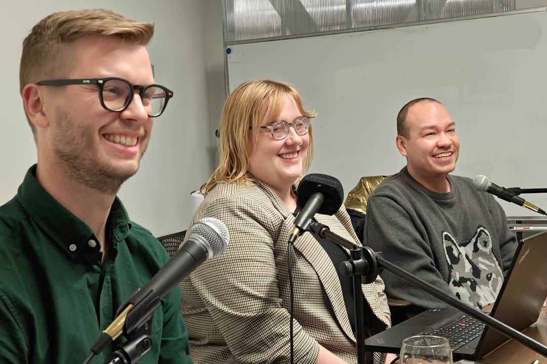 Three smiling people sit in a row with microphones before them.