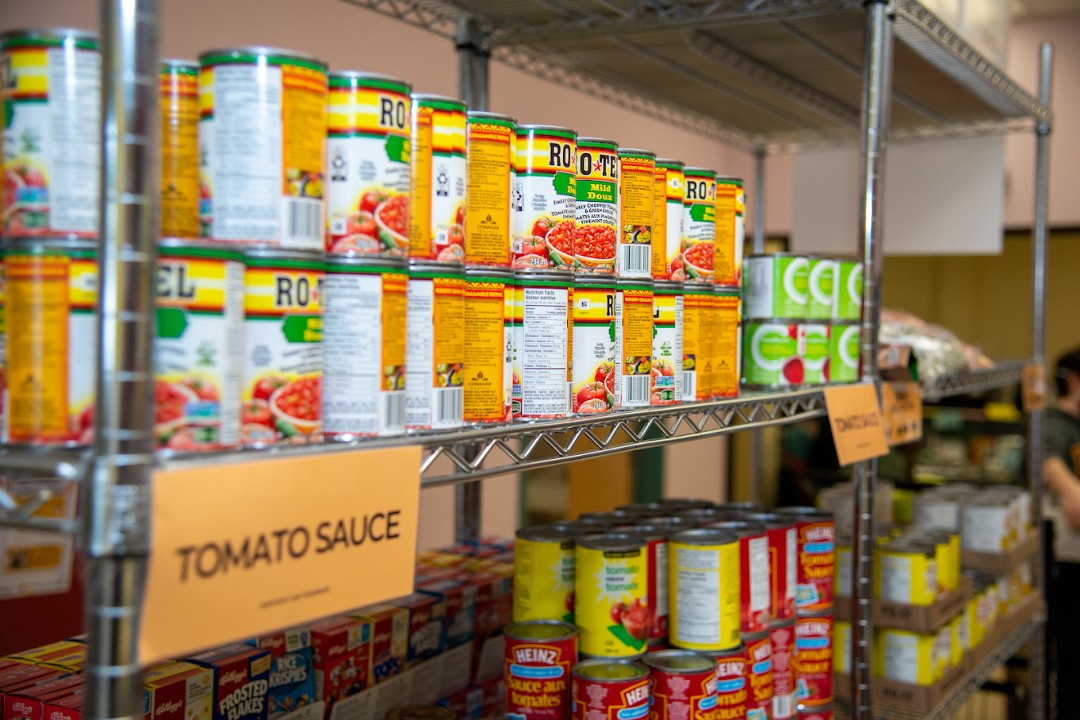 Shelves containing canned food and a sign that reads "Tomato sauce".
