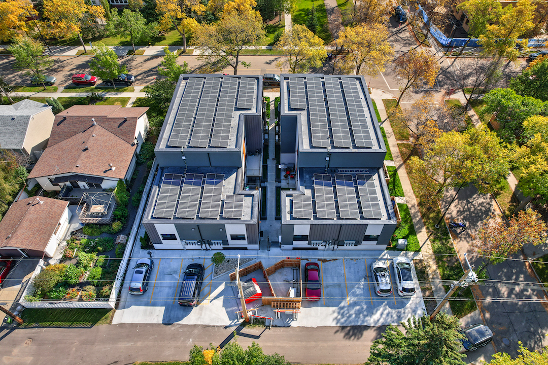 An aerial view of a multifamily housing development next to a single-family home.