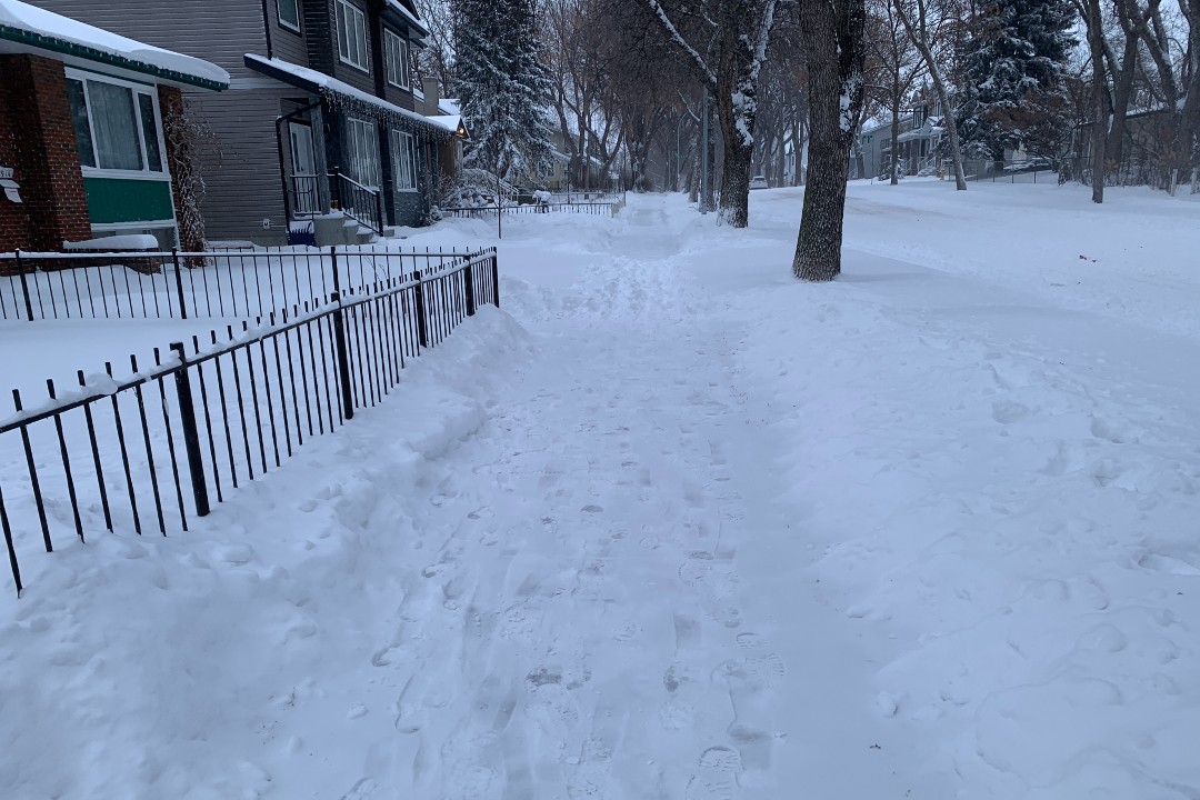A photo of a city sidewalk with snow cleared from most of it and a portion left unshovelled