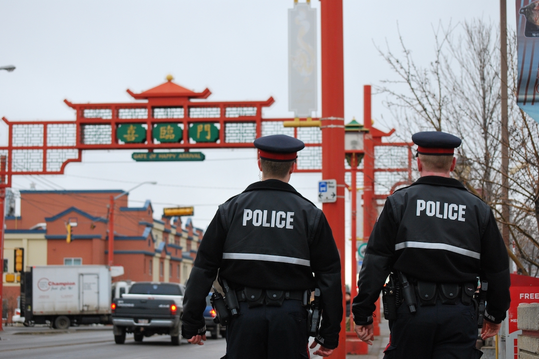 Two police officers are pictured from behind as they stand in front of a cultural gate in Edmonton's Chinatown.