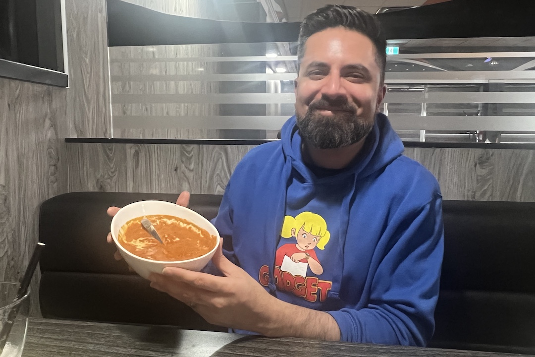 A person smiles while holding up a dish of butter chicken.