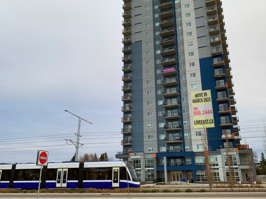 A photo that shows an LRT running beside a tall residential building in Edmonton
