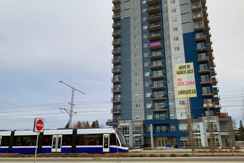 A photo that shows an LRT running beside a tall residential building in Edmonton