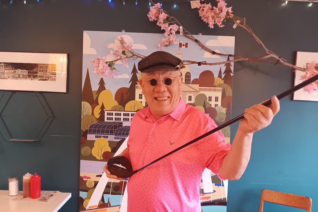 A person holding a golf cub poses in a restaurant in golf attire.