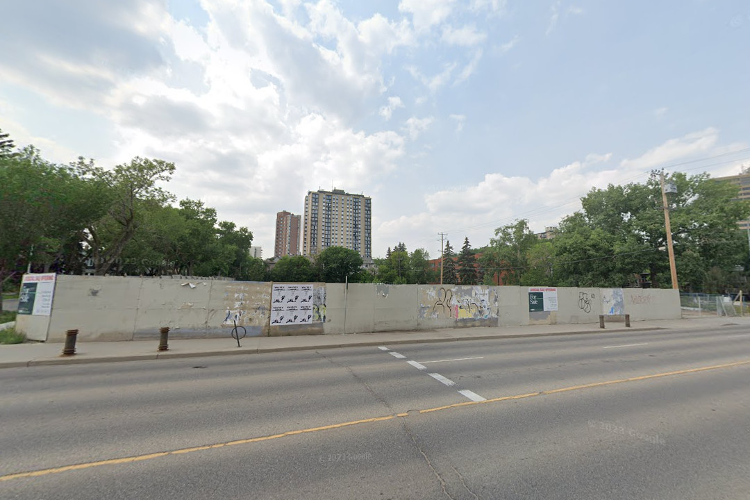 A vacant lot with a concrete barrier set up around it, viewed from the far side of the street