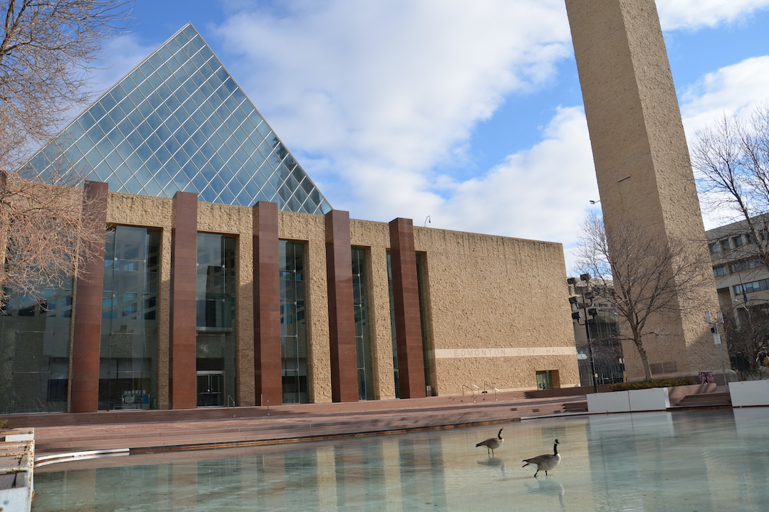 Two geese walk on ice in front of Edmonton City Hall.