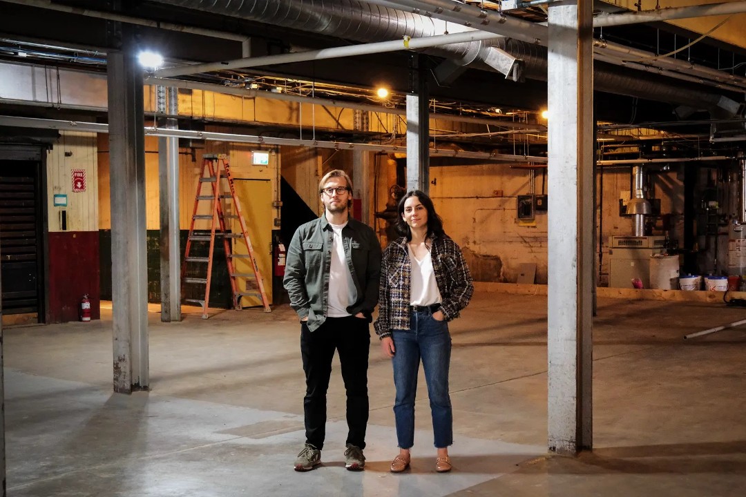 Two people stand inside a large but empty factory.