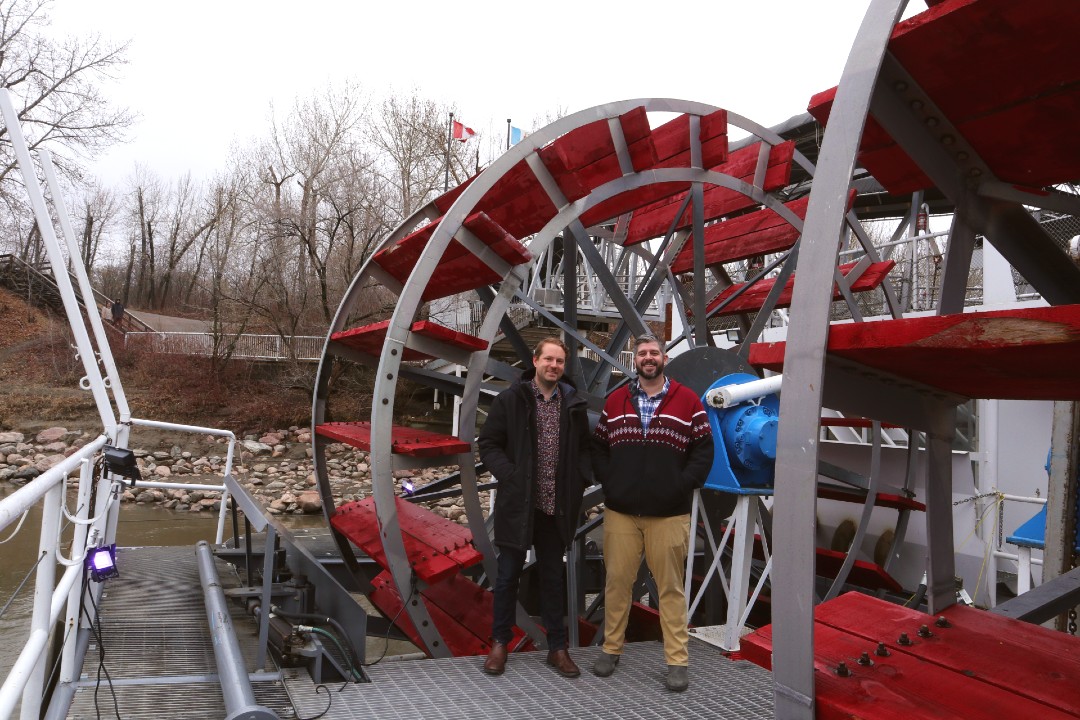 Two men stand by the paddles of the Edmonton Riverboat.