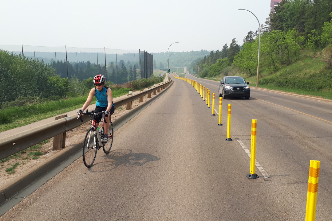 A cyclist pedals uphill in a road lane with bollards separating them from traffic.