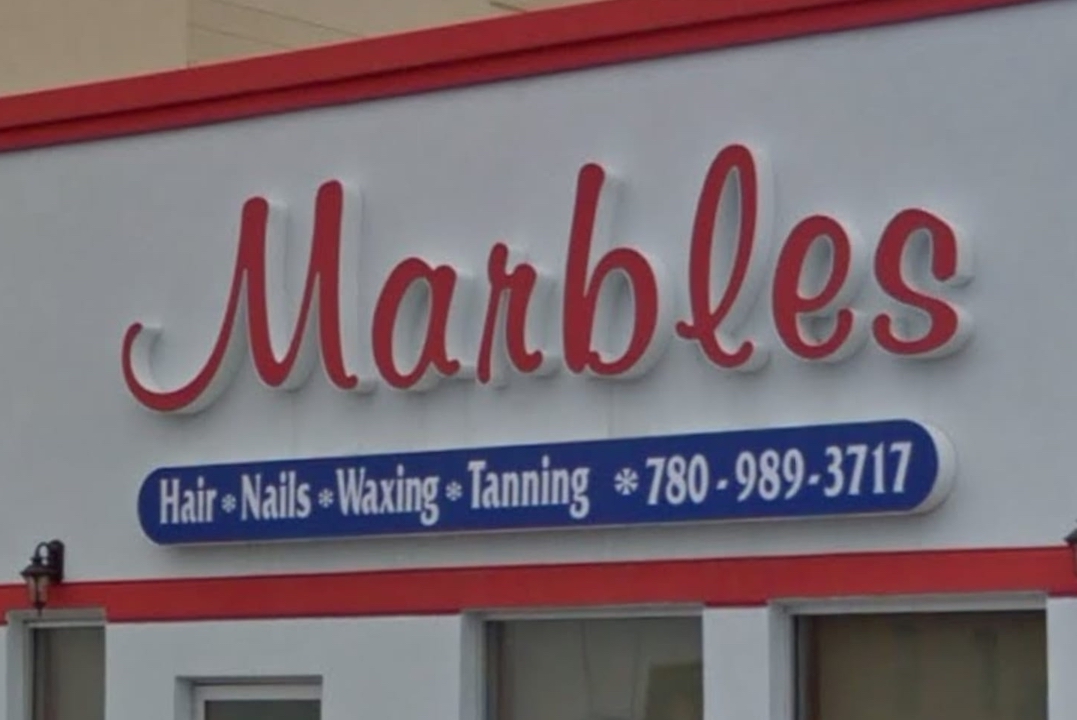 A picture of a façade of a business called Marbles that displays its name, services, and phone number.