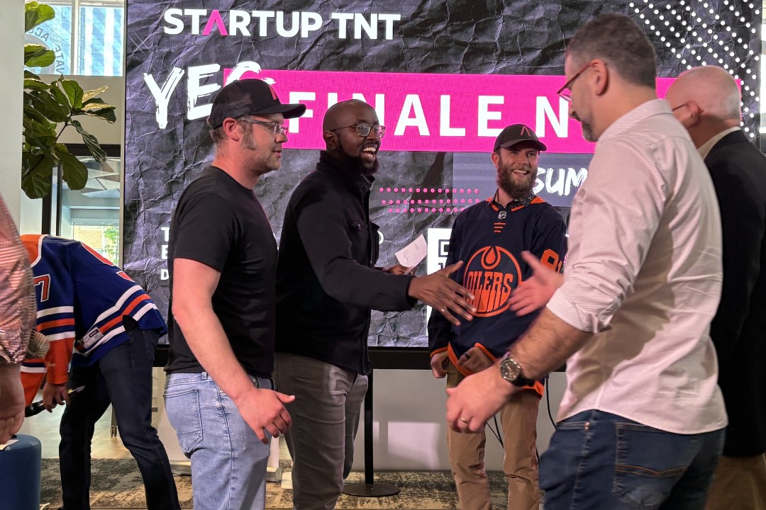 A person extends their hand to shake another's hand in front of a screen that says "Startup TNT"