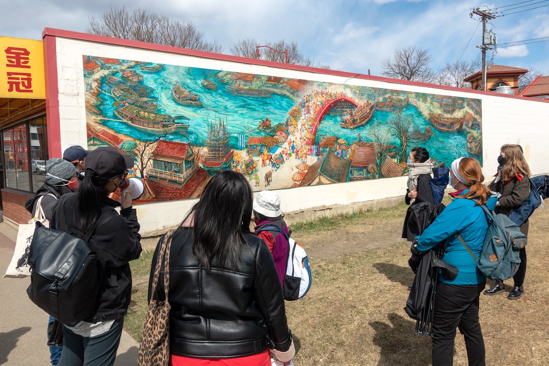 A group of people gather outdoors in front of a mural.