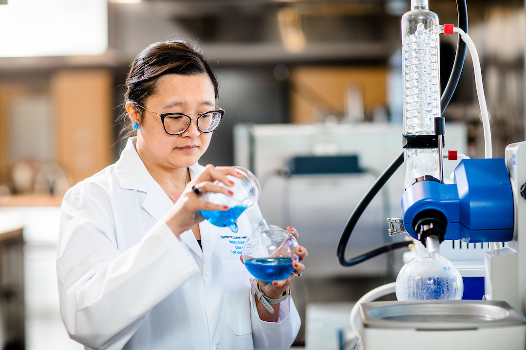 A scientist wearing a lab coat pours liquid into a beaker.