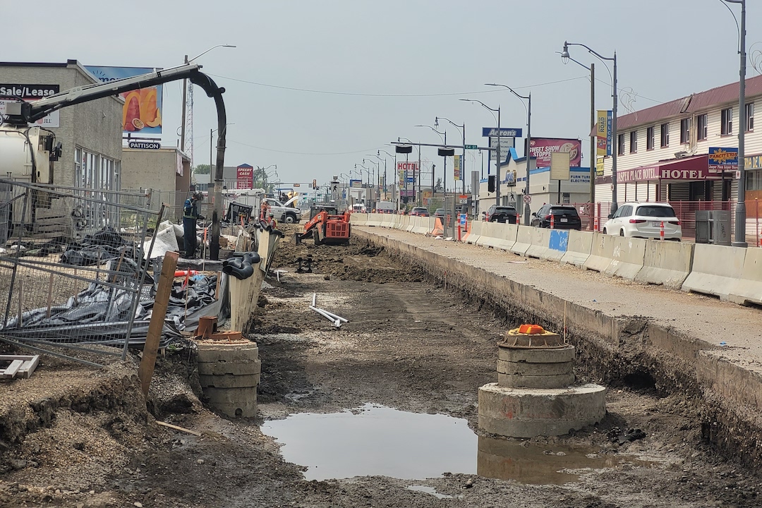 A muddy construction site flanked by businesses.