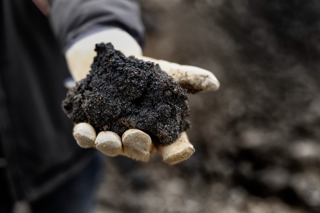 A person wearing a work glove holding bitumen.