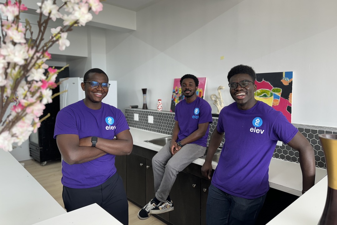 Three people in shirts that read "Elev" pose in a kitchen.