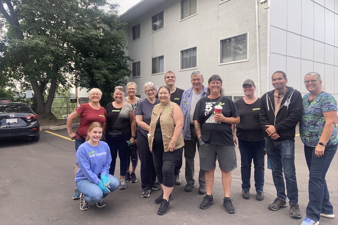 A group of smiling people pose in a parking lot outside an apartment building.