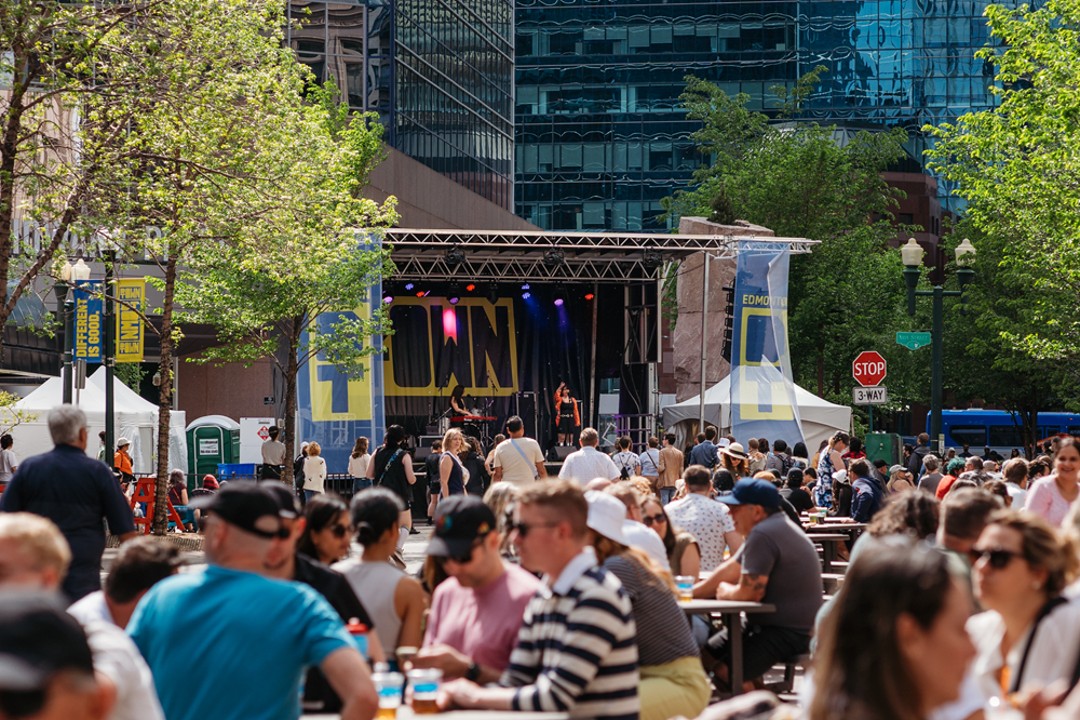 People sit at picnic tables with a music stage in the background.