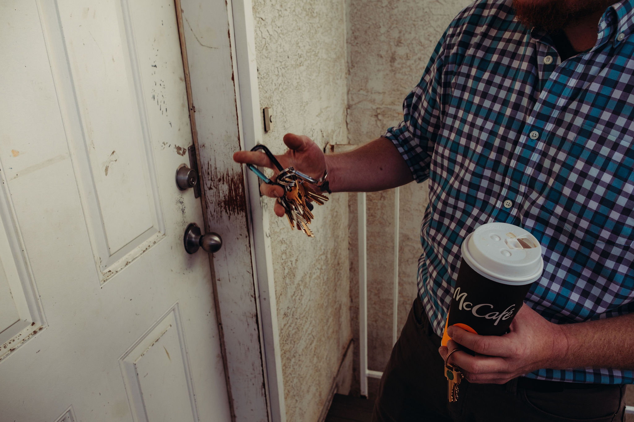 McDonald's coffee in hand, a man with a ring full of keys looks for the one to open the lock of a well-worn door.