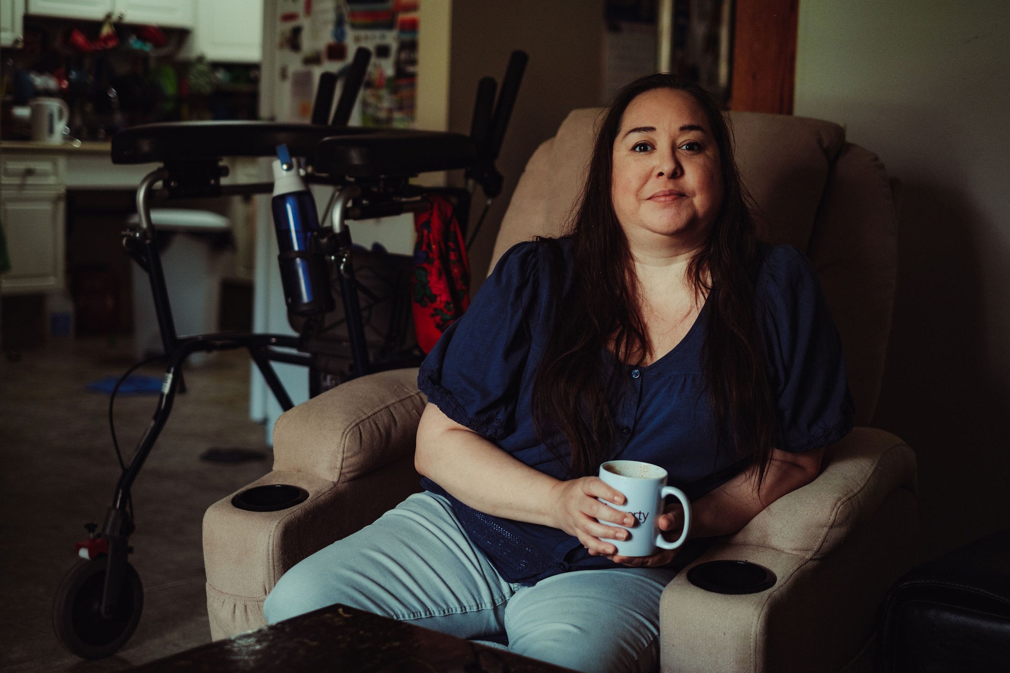 A woman sits on a chair holding a mug.